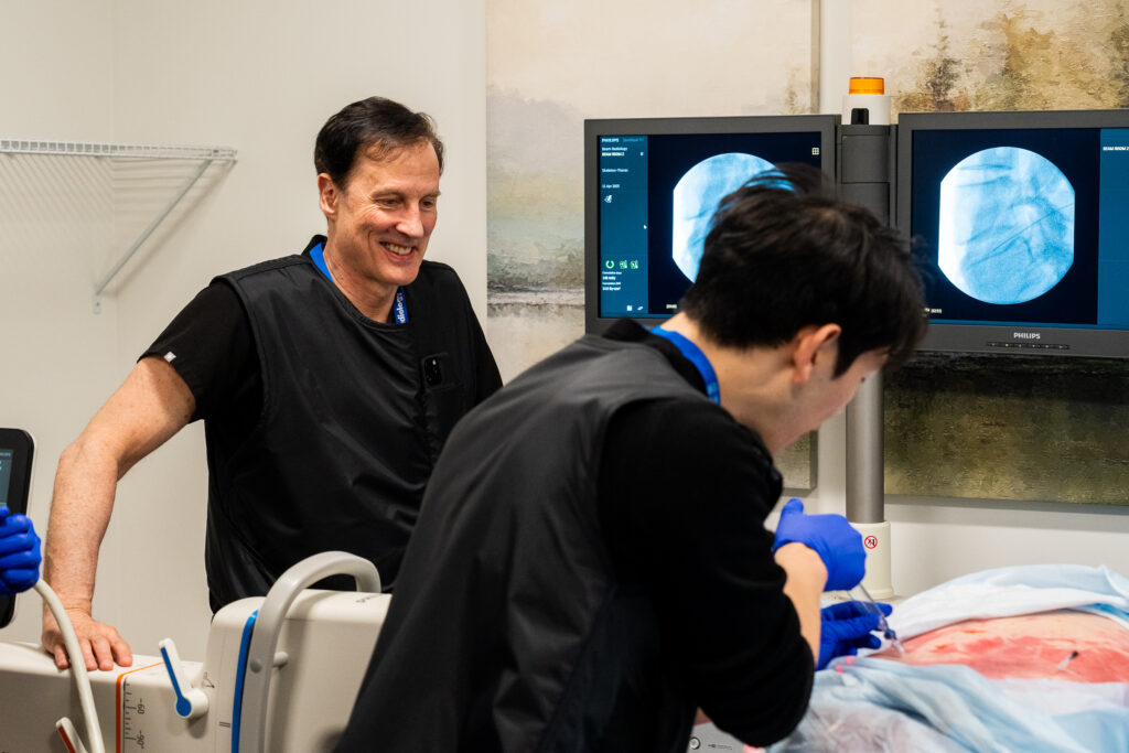 A medical professional in blue gloves performing a spine procedure on a patient